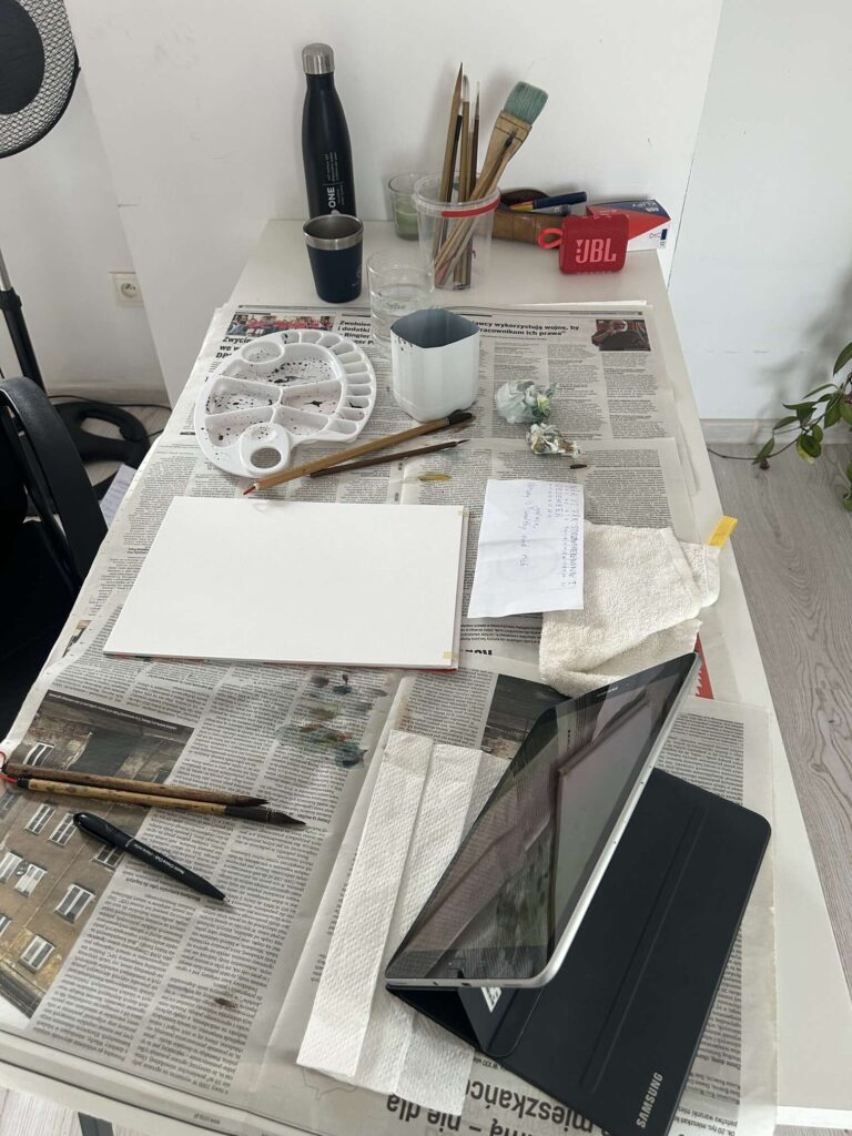 Zdjęcie: ujęcie stołu warsztatowego z góry. Przybory plastyczne rozrzucone po stole. 